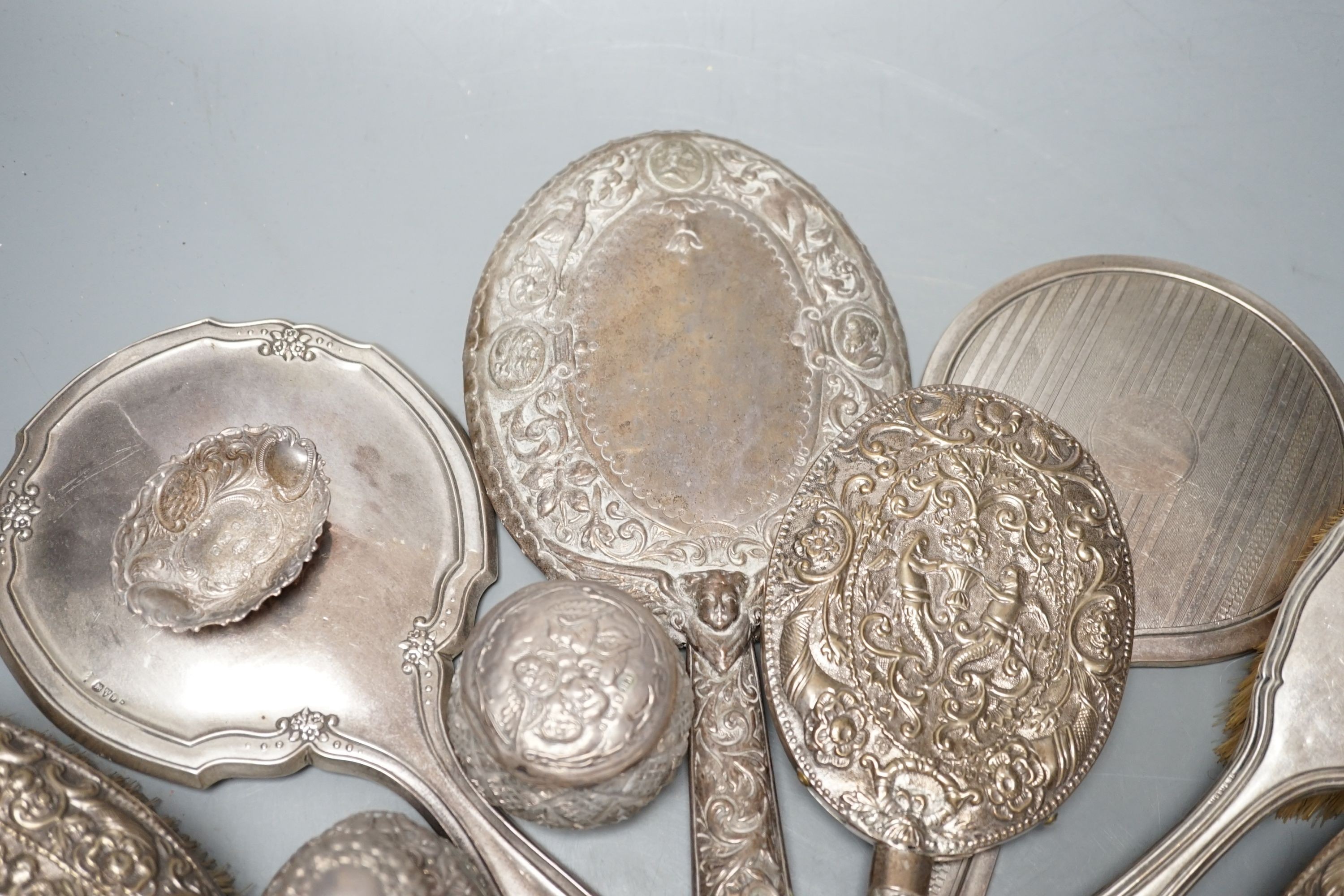 A mixed collection of four silver mounted vanity mirrors, four assorted clothes brushes, (including set of three), three silver mounted glass jars and a small silver dish.